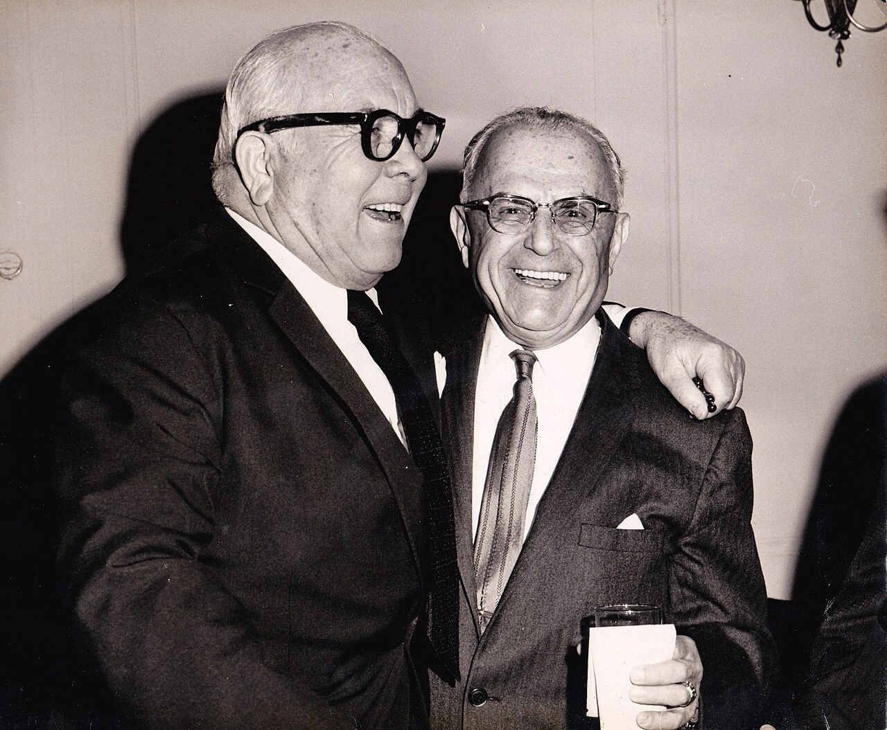 Black-and-white photograph of Spyros Skouras smiling in a suit at an event, standing beside another man with an arm arou